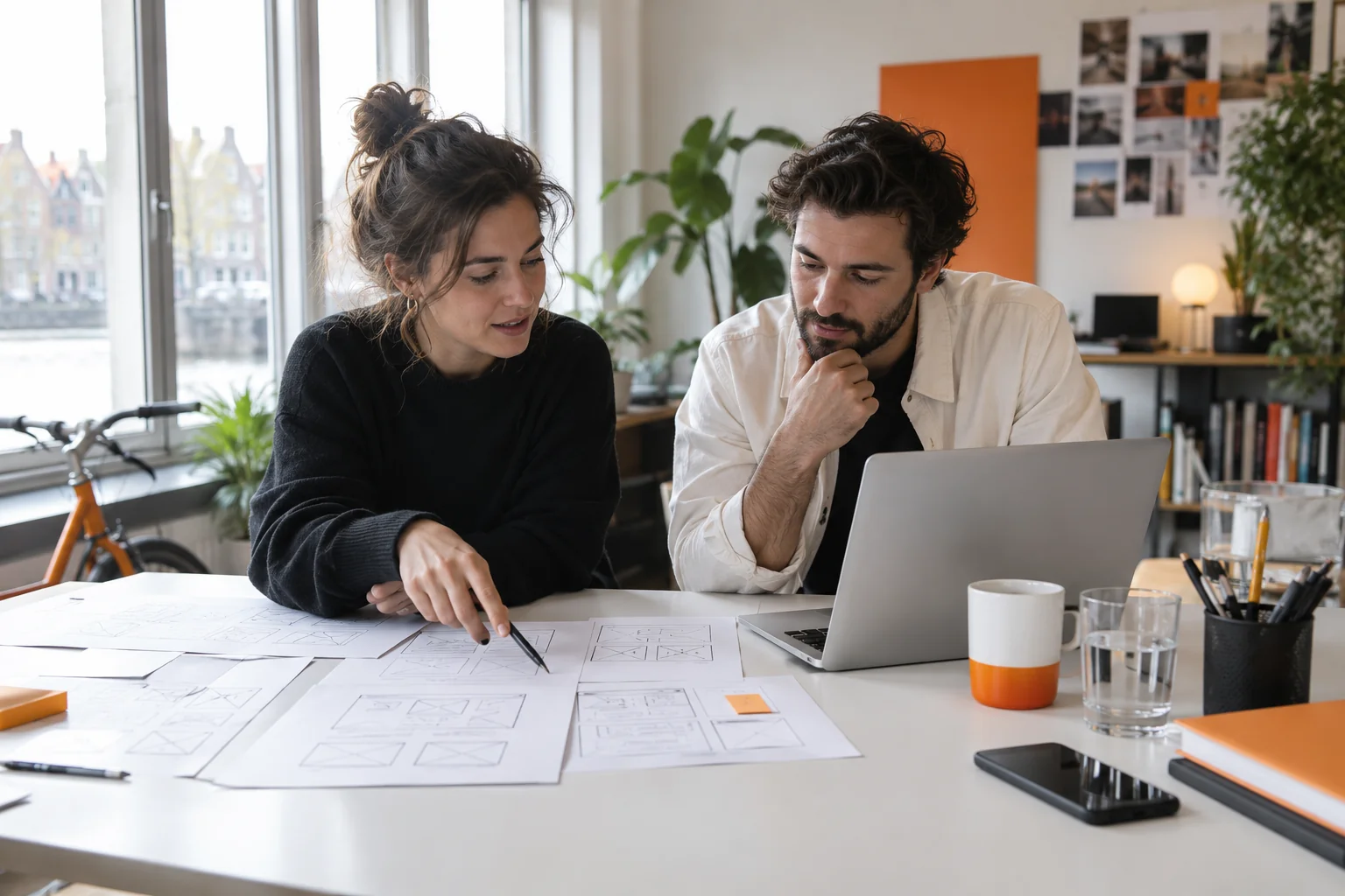 Ontwerper en ondernemer bespreken samen schetsen aan een lichte werktafel